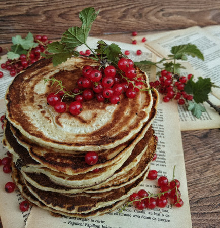 Fresh tasty pancakes with red currants on the old papers on a wooden tableの写真素材