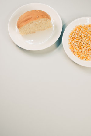 A vertical shot of half bread bun and corn grains on a plate isolated on white backgroundの写真素材