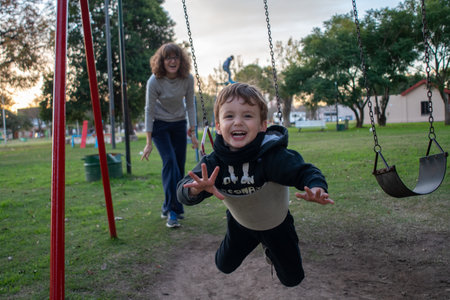 A cute happy male child being pushed by his mother on a swingの写真素材