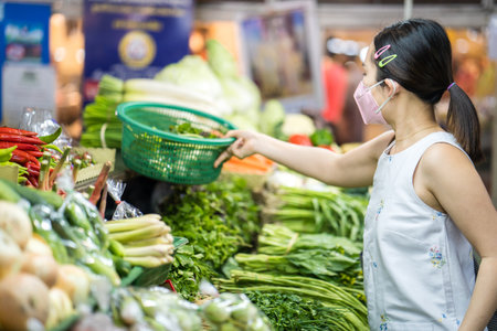 A Thai female in a protective face mask buying vegetables at the marketの写真素材