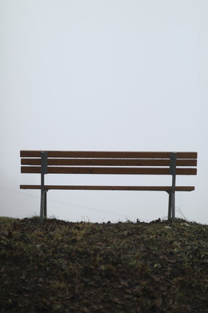 A vertical shot of a bench in a park under a cloudy sky on a gloomy dayの写真素材