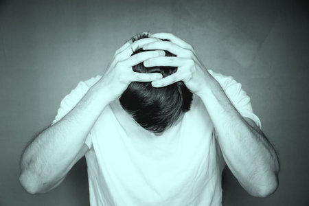A grayscale shot of a man holding his head with his hands, feeling distraught and stressedの写真素材