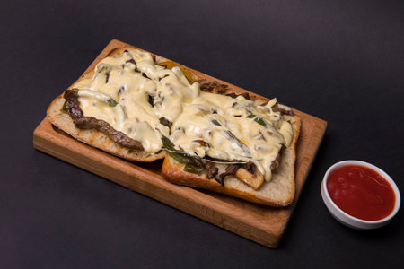 Two bread slices with beef and melted cheese served on a wooden board with a ketchupの写真素材