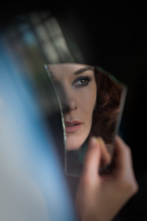 A vertical shot of an elegant European woman from Germany holding a broken piece of mirrorの写真素材