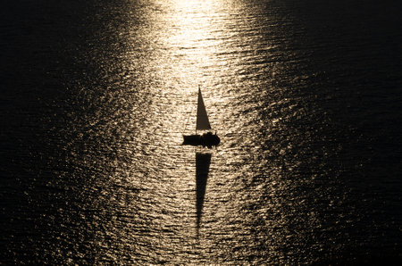 An aerial greyscale shot of a sailing boat in the middle of the endless oceanの写真素材