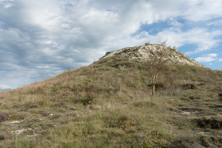 A low angle shot of a hill covered in dried grass under the cloudy skyの写真素材