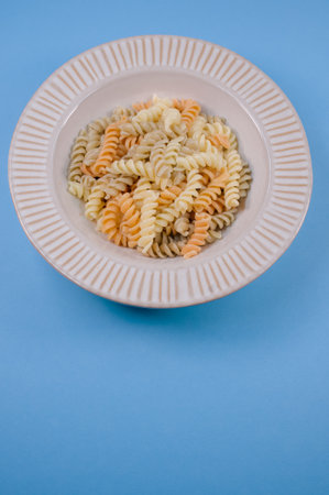 A plate with pasta twists isolated on a blue background with free space for textの写真素材