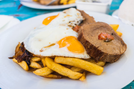 A closeup of a plate full of fries, cooked meat, and eggsの写真素材
