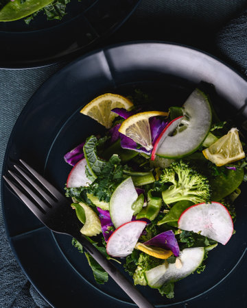 A vertical top view of a delicious colorful summer salad on a black plate with a fork next to itの写真素材