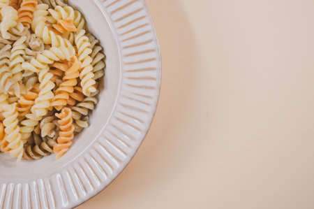 A plate with pasta twists isolated on a beige background with free space for textの写真素材