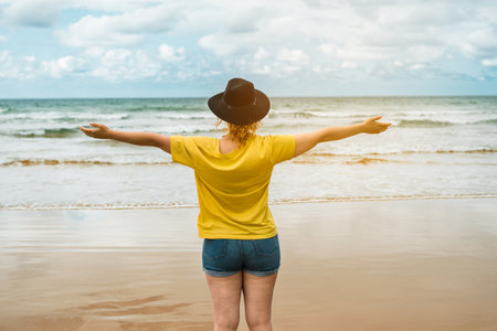 A caucasian female in a yellow t-shirt with open arms at the beachの写真素材