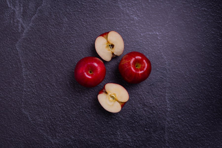 A top view of sliced and whole red apples on a gray surface