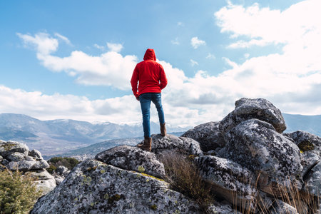 A male standing on the rocks looking at the mountains under a cloudy skyの写真素材
