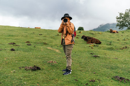A caucasian female in an orange coat and a hat taking a photo of the camera in a fieldの写真素材