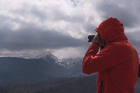A photographer in a red coat taking a photo of a landscapeの写真素材
