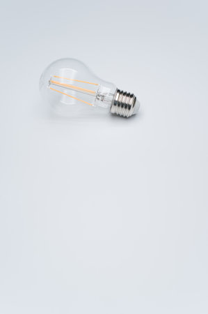 A vertical closeup of a light bulb on light gray background.