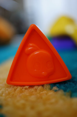 An orange triangle plastic toy with a cute duck on a carpeted in children room