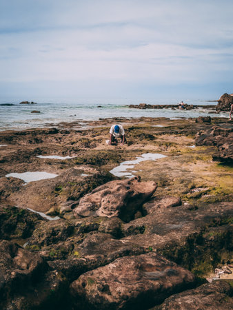 A vertical shot of the person kneeled looking down on the beach surrounded by rocks in Portugal.の写真素材
