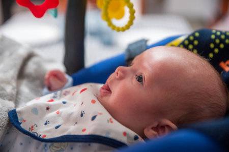 A closeup shot of a cute baby boy in a rocking chair looking at hanging toys