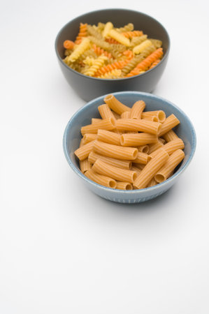 A vertical shot of tri-color rotini and rigatoni pasta on a bowl isolated on white backgroundの写真素材