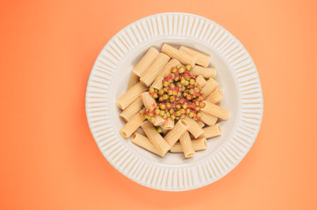 A top view of rigatoni pasta with green peas on a plate isolated on an orange backgroundの写真素材