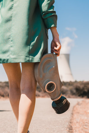 A closeup view of a person holding an anti gas mask walking into the factory on a sunny dayの写真素材