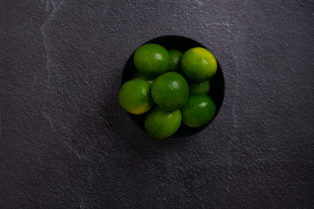 A top view of green limes in a bowl on a gray surfaceの写真素材