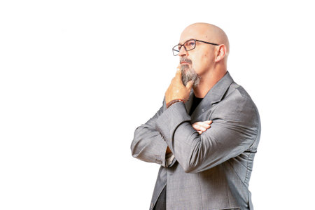 A thoughtful bald male in an elegant gray suit standing against an isolated white background