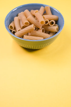 A vertical shot of uncooked rigatoni pasta on a bowl isolated on yellow backgroundの写真素材
