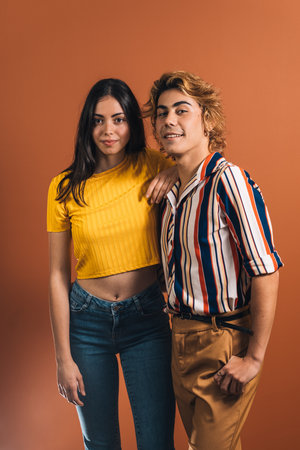 A young stylish couple wearing colorful clothes standing in the background of an orange wallの写真素材
