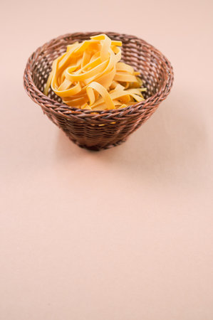 A vertical shot of uncooked fettuccine pasta on a wicker bowl isolated on brown backgroundの写真素材
