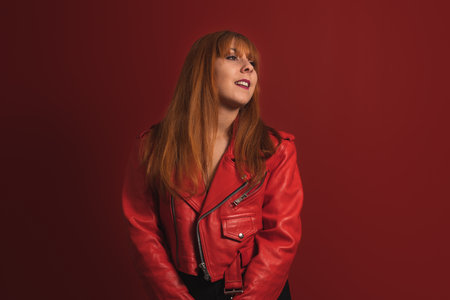 A smiling caucasian female in a red jacket posing on the red backgroundの写真素材