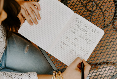 A closeup shot of a South Asian woman in the cafe writing something in the copybookの写真素材