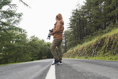A caucasian female with a camera standing in the middle of a road looking at the viewの写真素材