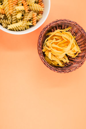 A vertical shot of tri-color rotini and fettuccine pasta on a bowl isolated on an orange backgroundの写真素材