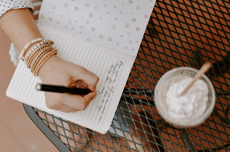 A closeup shot of a South Asian young woman writing something in the copybook sitting in the cafeの写真素材