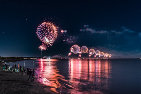 Fireworks shot at the same time from the seashore and people watching from the beach
