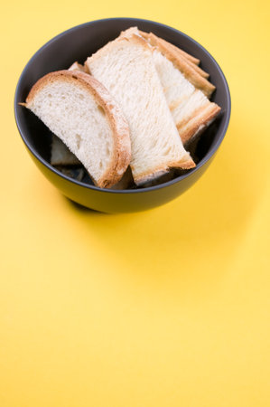 A vertical shot of bread slices on a bowl isolated on yellow backgroundの写真素材