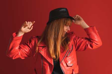 A smiling caucasian female in a red jacket and hat posing on the red backgroundの写真素材