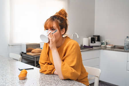 A closeup shot of a caucasian female drinking tea in a kitchenの写真素材