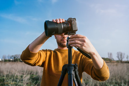 A caucasian male in a yellow sweater fixing a camera to take a photo of the viewの写真素材