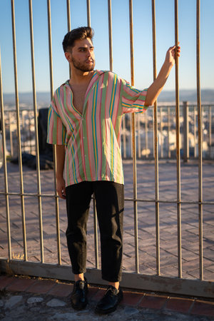 A vertical shot of a sexy young Caucasian male in a stylish outfit posing in sunny townの写真素材