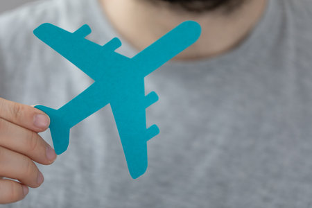 A person's hand holding a blue paper cut in an airplane shape