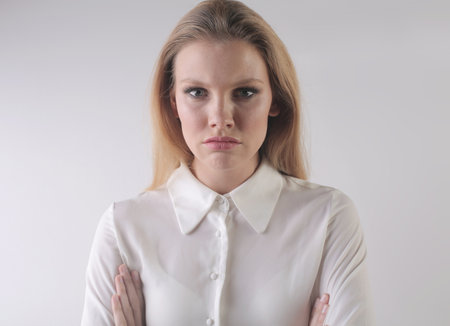A portrait of an angry young blonde female with crossed arms on a white backgroundの写真素材