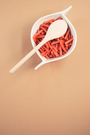 A bowl of macaroni pasta with a wooden spoon isolated on orange background with free space for textの写真素材