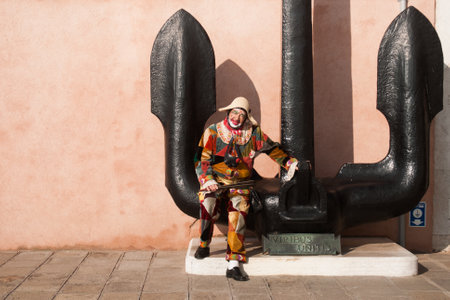 A male wearing a carnival costume sitting on the anchor statue in Venice, Italyの写真素材