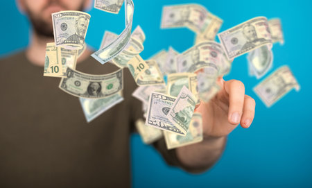 A closeup of US paper bills flying in the air with a man holding out his hand in the backgroundの写真素材