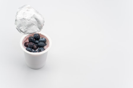 A high angle shot of a cup of yogurt with fresh berries on a white surface