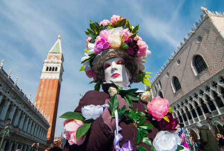 A female in a carnival mask and costume with flowers standing on the background of St Mark's Campanile in Venice, Italyの写真素材