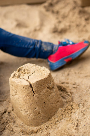 A vertical shot of a sand castle with a baby boy foot in the backgroundの写真素材